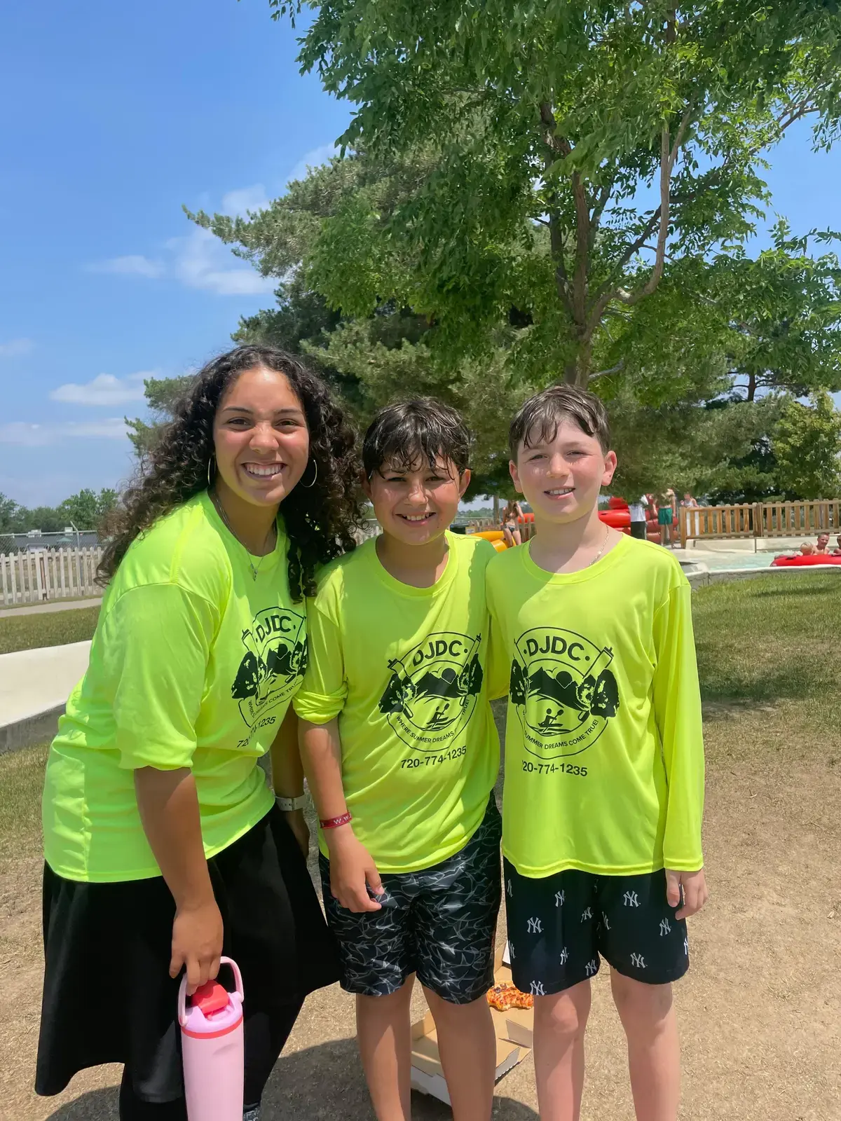 A counselor with two campers in neon camp shirts outside