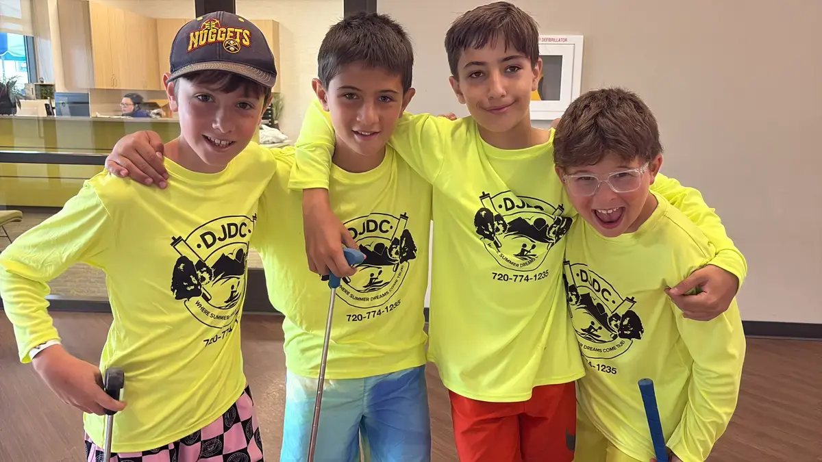 Two campers in neon DJDC shirts with golf clubs, laughing