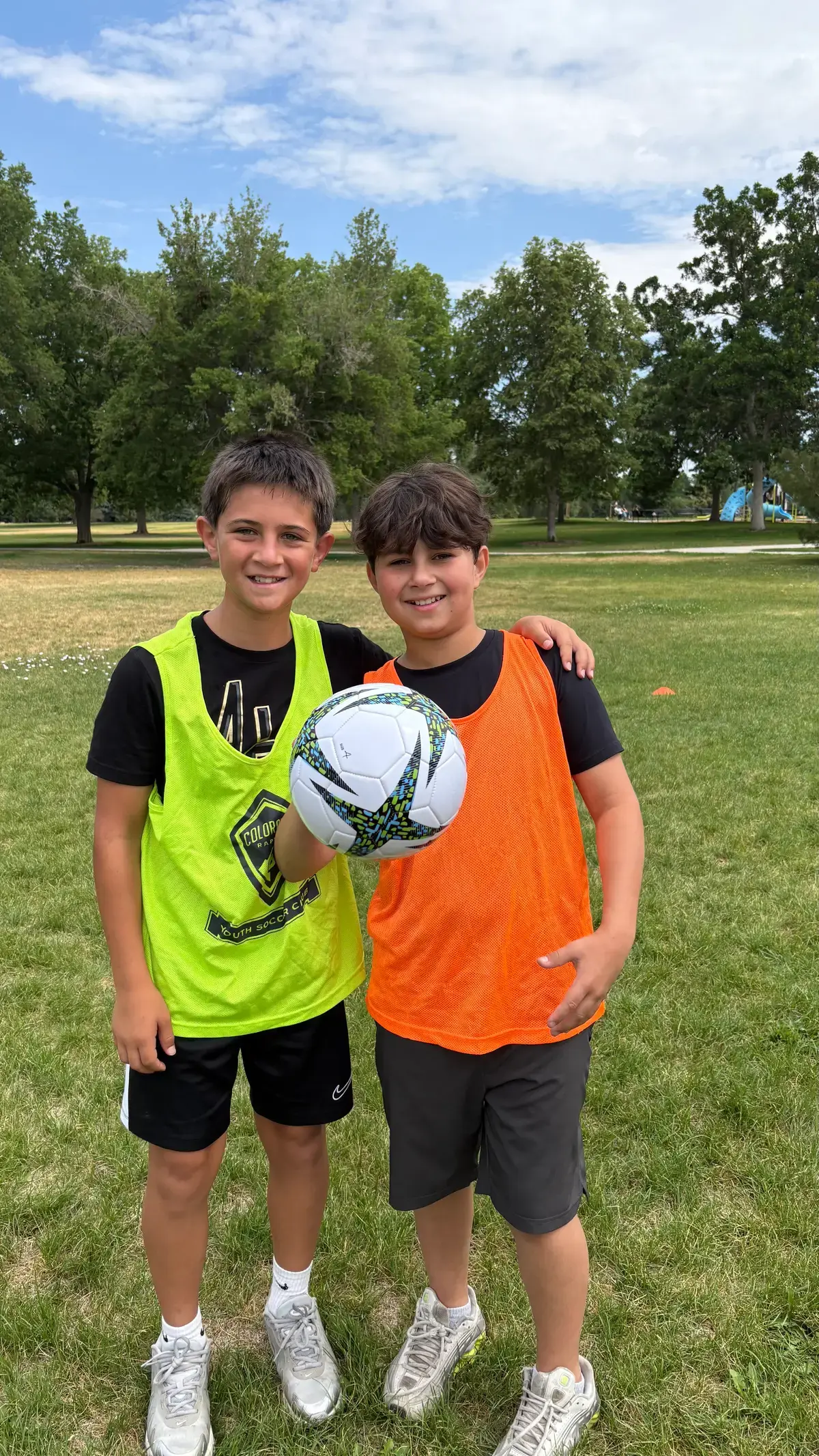Two friends with a soccer ball in orange pinnies