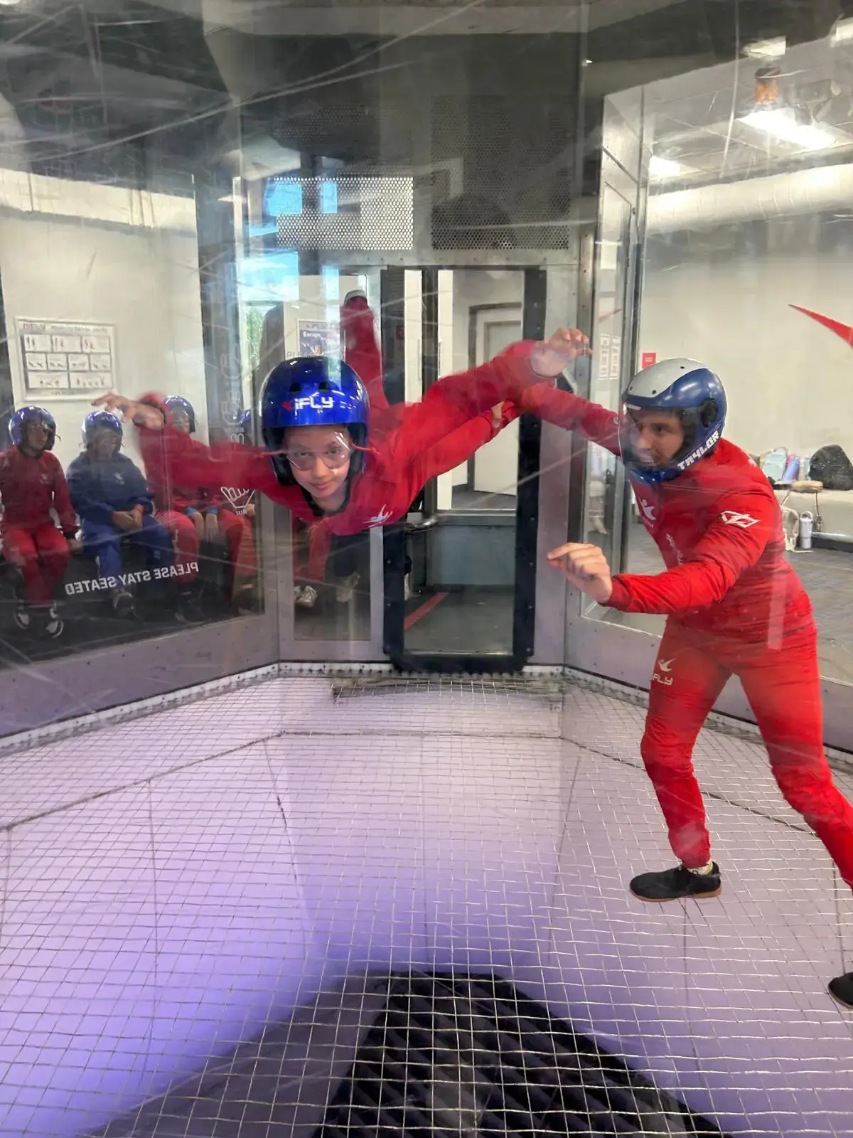 Camper flying in the iFly indoor skydiving wind tunnel with an instructor alongside